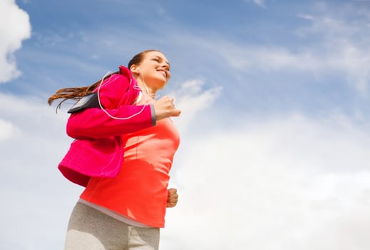 fitness, sport and lifestyle concept - smiling young woman with earphones running outdoors