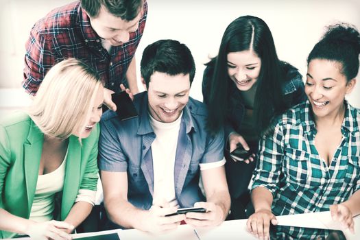 education concept - group of students looking into smartphone at school