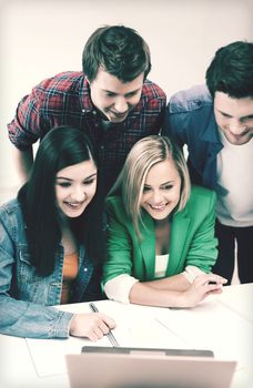 education concept - smiling students looking at laptop at school