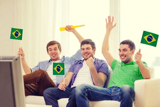 friendship, sports and entertainment concept - happy male friends with flags and vuvuzela supporting football team at home