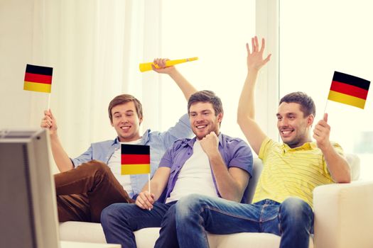 friendship, sports and entertainment concept - happy male friends with flags and vuvuzela supporting football team at home