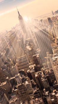 New York City. Manhattan downtown skyline with illuminated Empire State Building and skyscrapers at sunset. Vertical composition. Warm evening colors. 