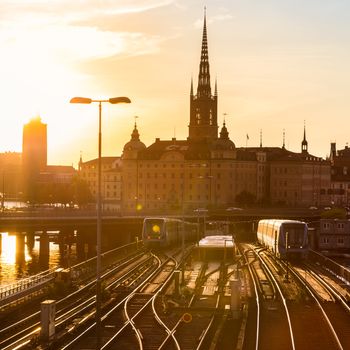 Railway tracks and trains near Stockholm's main train station in Norrmalm area, Stockholm, Sweden in sunset.  Silhouette of city hall and cathedral in background. Square composition.