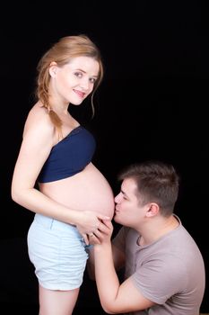 man kisses a woman's abdomen where the baby grows