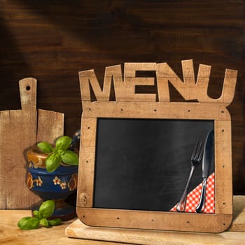 Empty blackboard with wooden frame and text Menu in the kitchen with mortar and pestle with basil leaves and cutting boards. Template for food menu