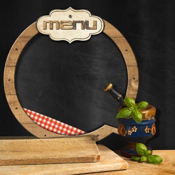 Empty round blackboard with wooden frame and label with text Menu, in the kitchen with mortar and pestle with basil leaves and cutting boards. Template for food menu