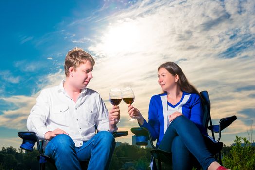 happy husband and wife with glasses on chairs at sunset