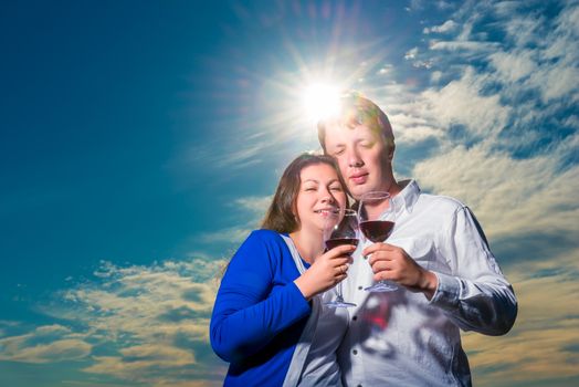 couple with glasses of wine embraces under the rays of the setting sun