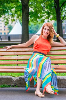 woman in a bright orange dress on a park bench