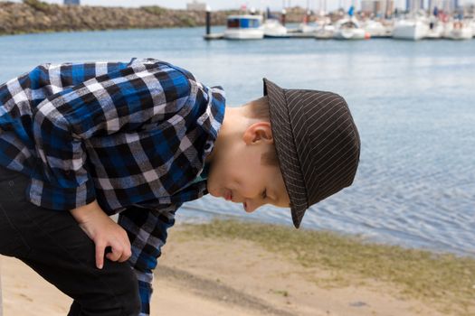 A young boy bending over to pick up rocks at the beach.