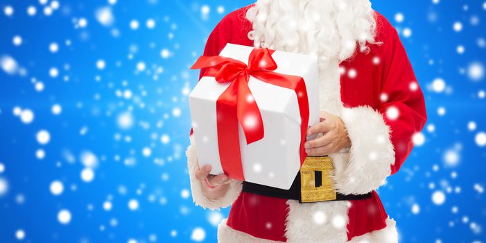 christmas, holidays and people concept - close up of santa claus with gift box over blue snowy background
