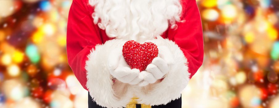 christmas, holidays, love, charity and people concept - close up of santa claus with heart shape decoration over red lights background