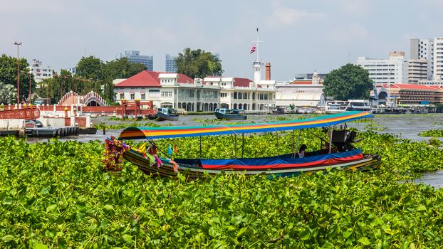 Tourist boat on the Chao Phraya River on the background of a harbor. City of Bangkok occupies 1.568 square kilometers with a population of 8 million inhabitants.