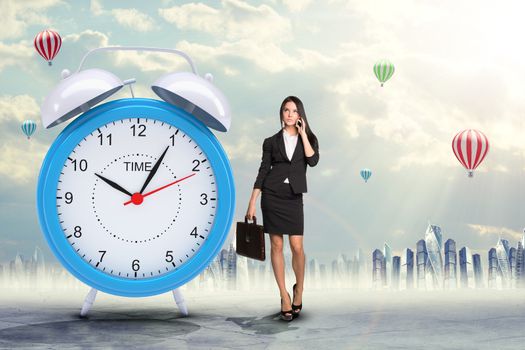 Lady talking on cell phone with big alarm clock on city background