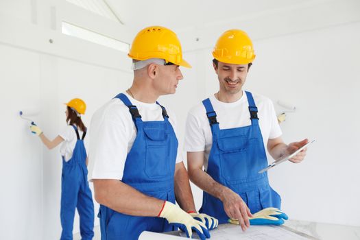 Construction workers looking at house plan and painting walls