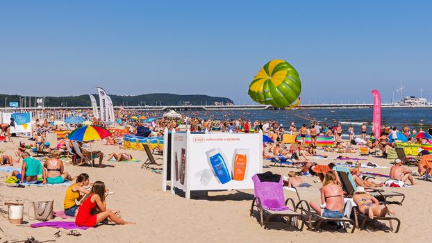 People sunbath on the beach in Sopot, major SPA and tourist resort on the Polish Baltic Sea coast. In the background the longest wooden pier in Europe at 511 m.