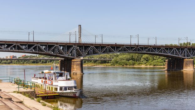 Pleasure boat moored at the boulevard along Vistula river in Warsaw. In the very background the Swietokrzyski Bridge, first modern cable-stayed bridge in Warsaw 479 m long.