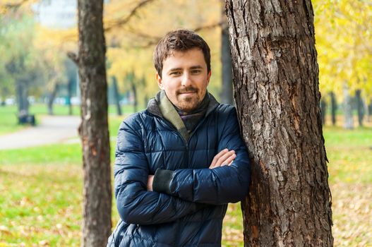 Handsome guy leaned against a tree in autumn park