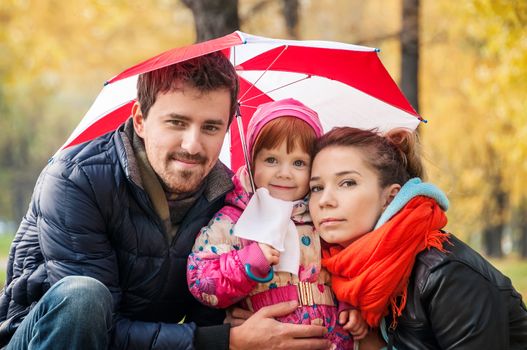 Happy young family under an umbrella in an autumn park