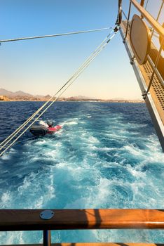 Wooden sailboat tows rubber boat in the sea