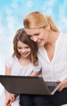 family, childhood, holidays, technology and people concept - smiling mother and little girl with laptop computer over blue lights background