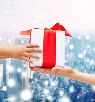 holidays, present, christmas, childhood and happiness concept - close up of child and mother hands with gift box over snowy city background