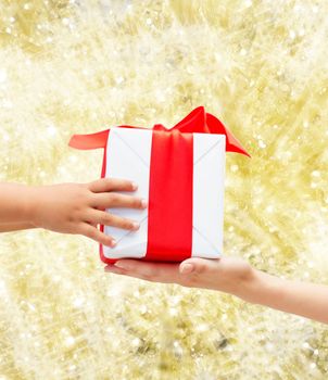 holidays, present, christmas, childhood and happiness concept - close up of child and mother hands with gift box over yellow lights background