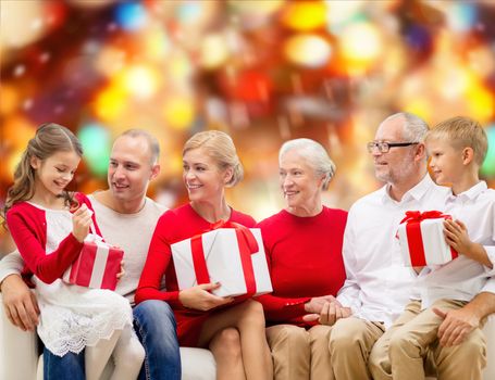 family, holidays, generation, christmas and people concept - smiling family with gift boxes sitting on couch over red lights background