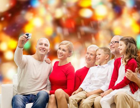 family, holidays, generation, christmas and people concept - smiling family with camera taking selfie and sitting on couch over red lights background