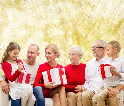 family, holidays, generation, christmas and people concept - smiling family with gift boxes sitting on couch over yellow lights background