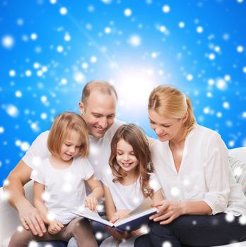 family, childhood, christmas holidays and people - smiling mother, father and little girls reading book over blue snowy background