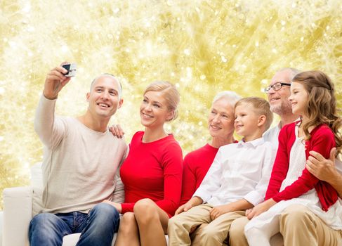 family, holidays, generation, christmas and people concept - smiling family with camera taking selfie and sitting on couch over yellow lights background