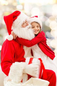 holidays, christmas, childhood and people concept - smiling little girl hugging with santa claus over lights background