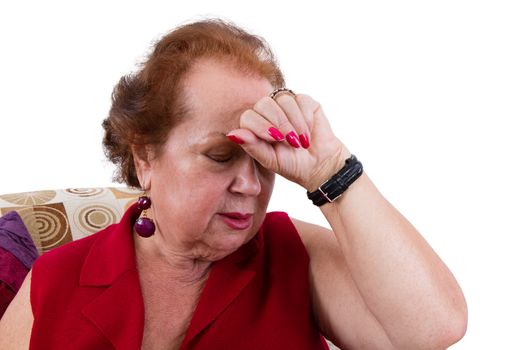 Senior lady having a bad day suffering from a headache holding her hand to her forehead as she closes her eyes against the pain, closeup view seated in an armchair isolated on white