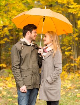 love, relationship, season, family and people concept - smiling couple with umbrella walking in autumn park