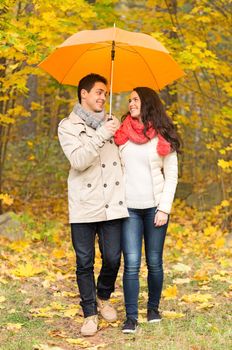 love, relationship, season, family and people concept - smiling couple with umbrella walking in autumn park