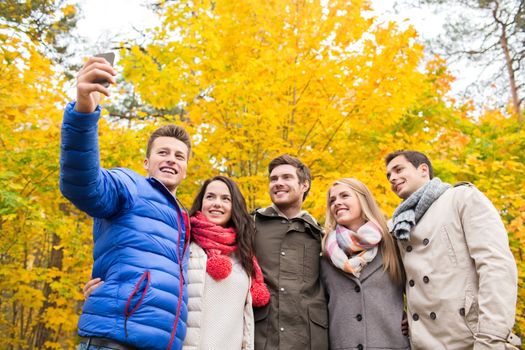 season, people, technology and friendship concept - group of smiling friends with smartphone taking selfie in autumn park