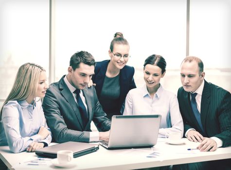 business, technology and office concept - smiling business team with laptop computers, documents and coffee having discussion in office