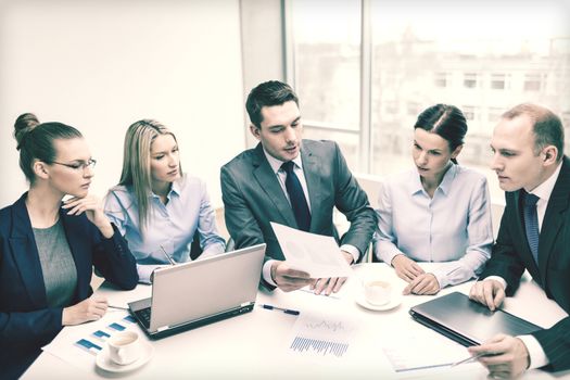 business, technology and office concept - smiling business team with laptop computers, documents and coffee having discussion in office