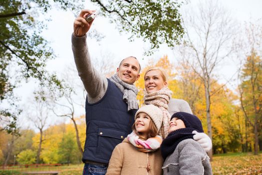 family, childhood, season, technology and people concept - happy family taking selfie with camera in autumn park