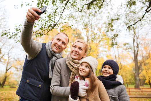 family, childhood, season, technology and people concept - happy family taking selfie with smartphone in autumn park