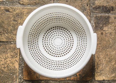 white colander for pasta on a rough bricked floor 