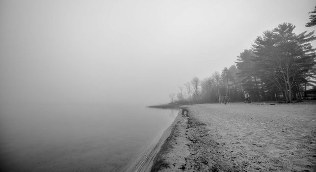 Black & white of lonely empty beach in November autumn fog in Ontario Canada.