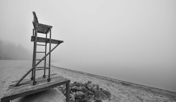 Black & white of lonely lifeguard seat stands empty in the fog on a November beach in Ontario Canada.