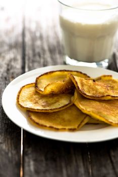 Homemade pancakes in plate on wooden table with glass of milk on background