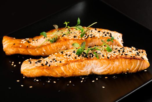 Fried salmon with sesame seeds and herbs on black plate close up