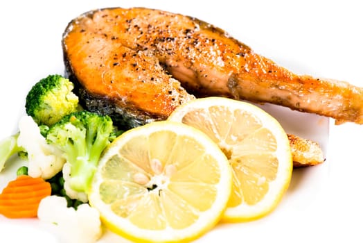 Fried salmon steak with vegetables and lemon on white