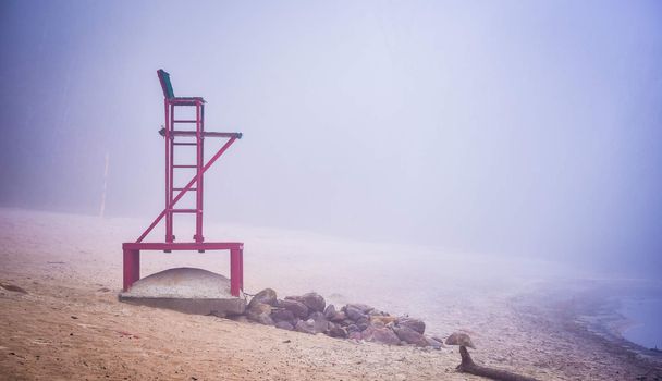 A lonely lifeguard seat stands empty in the fog on a November beach in Ontario Canada.