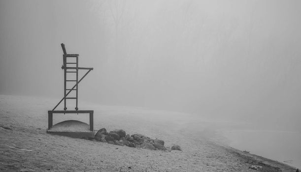 Black & white of lonely lifeguard seat stands empty in the fog on a November beach in Ontario Canada.