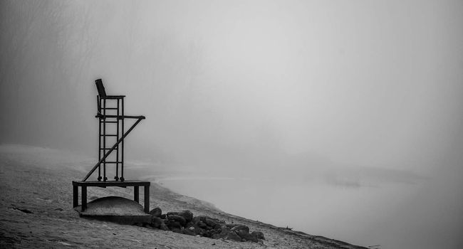 Black & white of lonely lifeguard seat stands empty in the fog on a November beach in Ontario Canada.